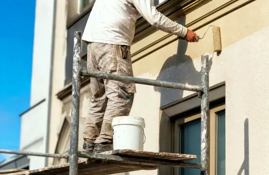 Painter on scaffolding repainting stucco at a Gardena shopping plaza